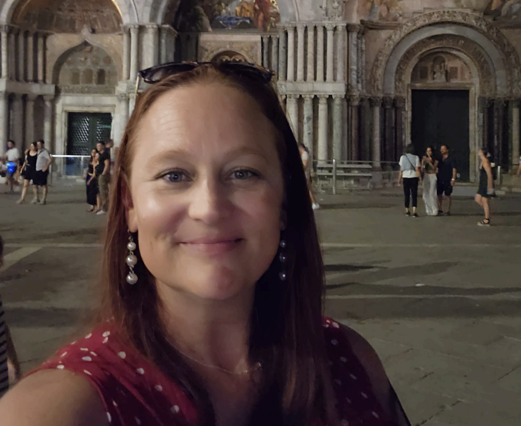 Smiling person taking a selfie in front of a historic building at night with ornate arches and columns.